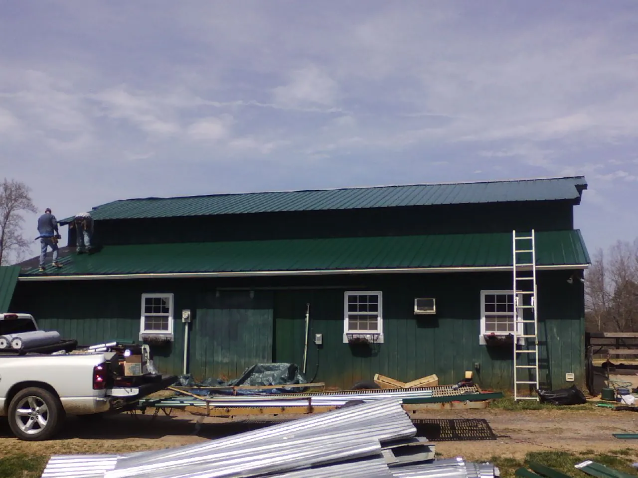 Crew installing green metal roofing on a large green barn in Saint Francis