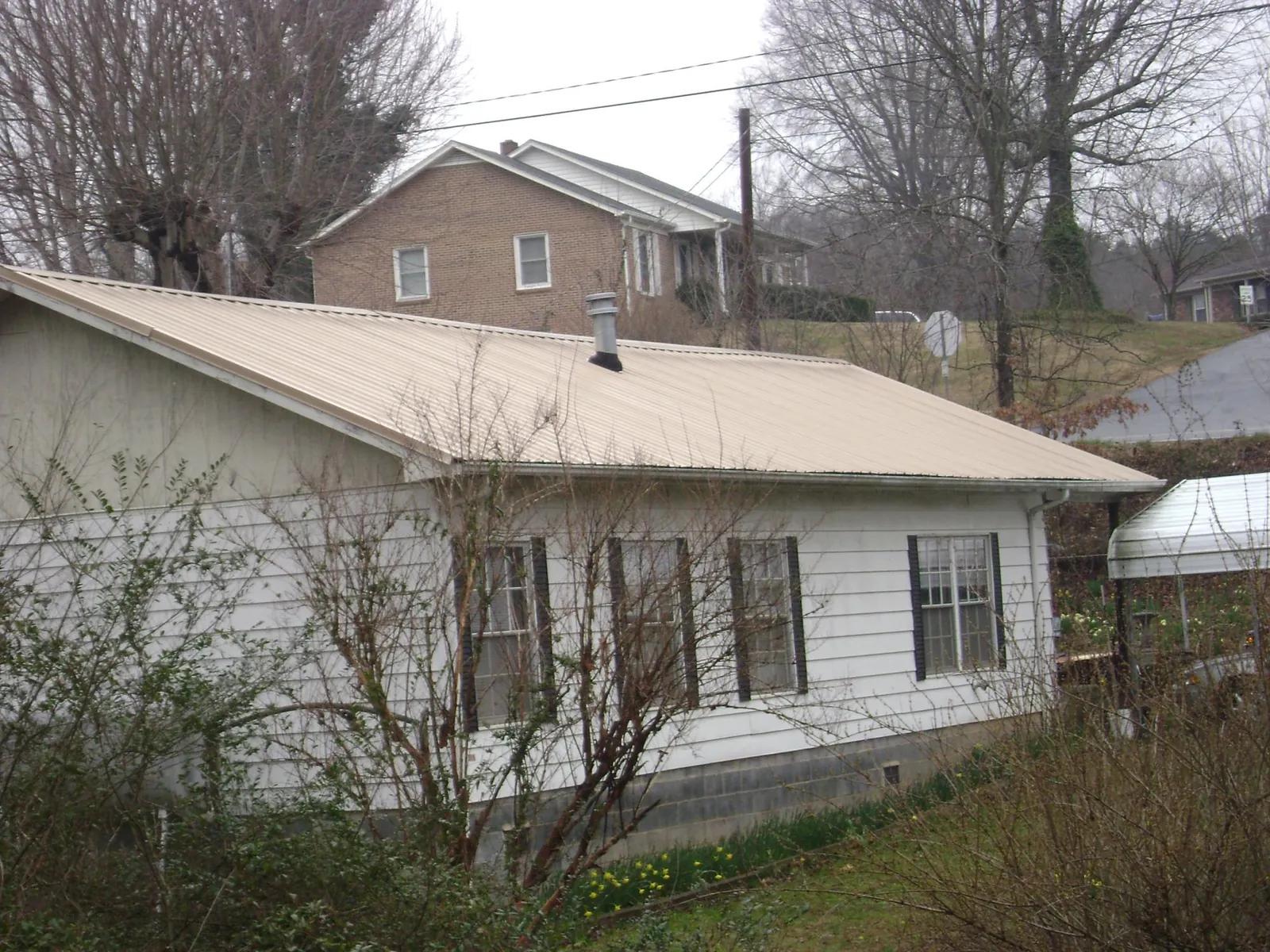 Tan metal roof on a white sided house set into a hillside — Commercial Roofing by Roofing Brothers in Saint Francis