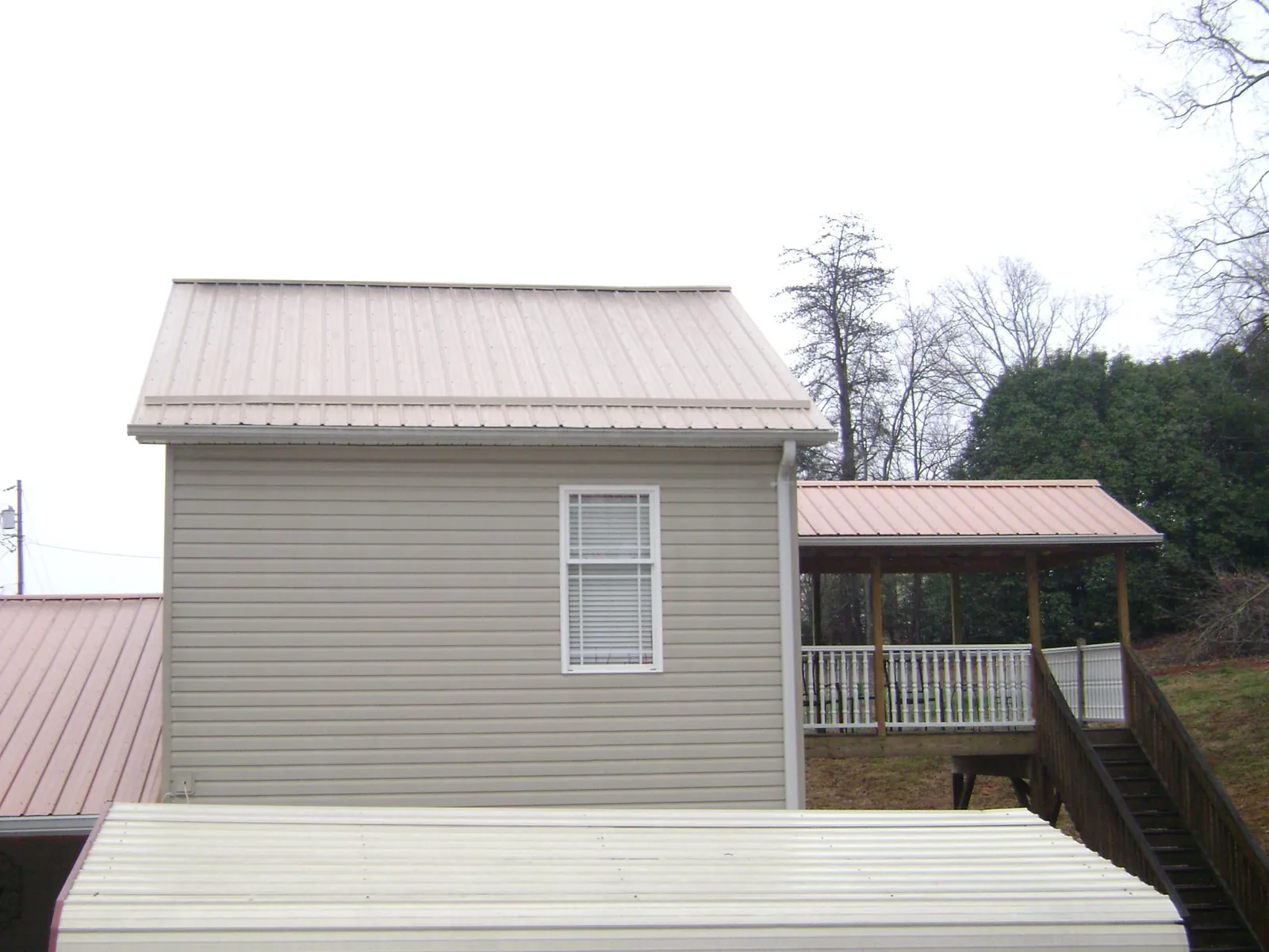 Tan metal roofs on a two story addition and attached porch, from a Roof Replacement job in Saint Francis